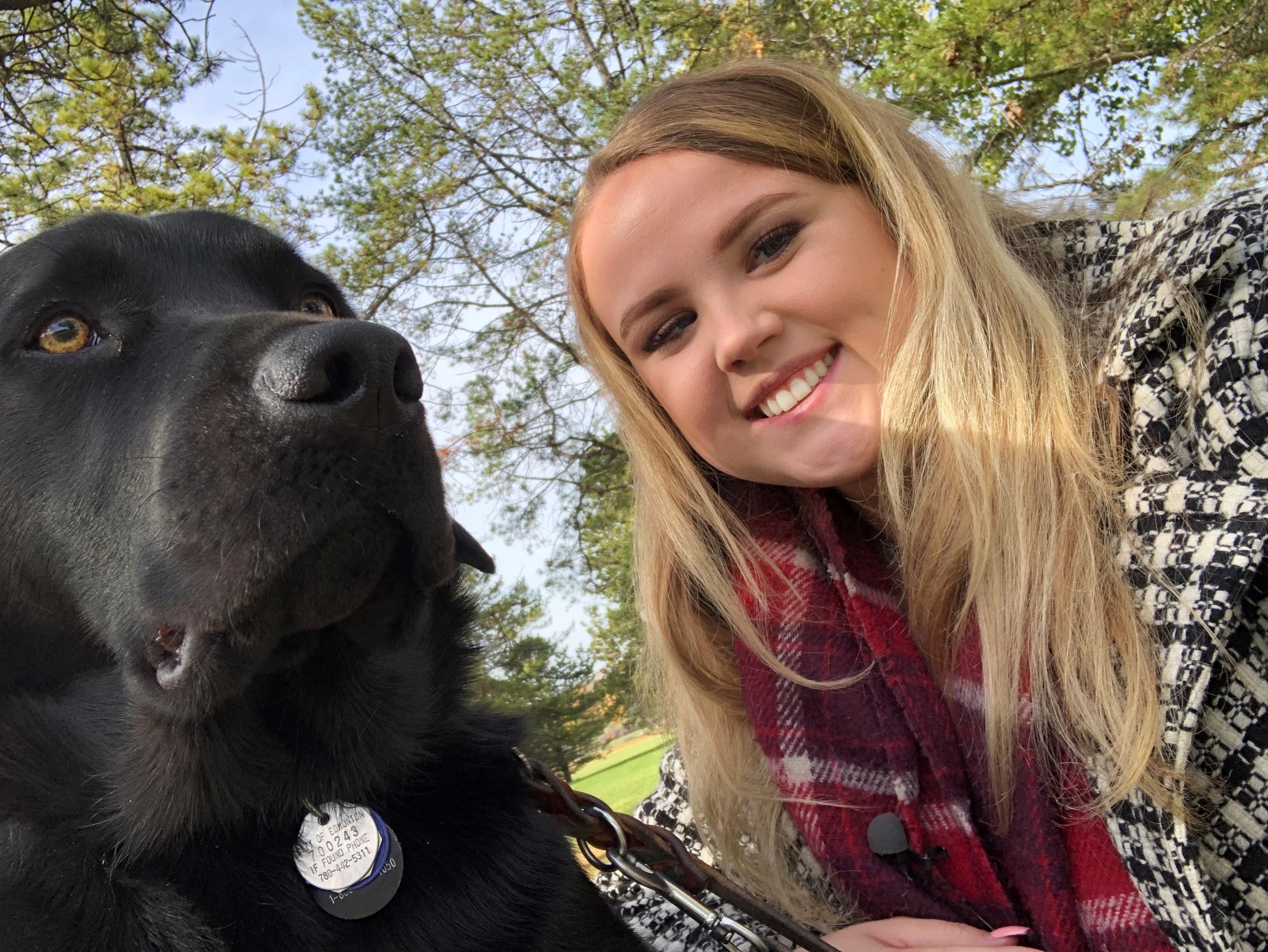 A woman smiles into the camera. A guide dog sits next to her.