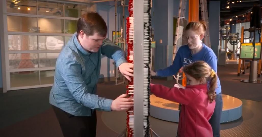 A man and little girl stand on either side of a pixel board, pushing plastic pins.