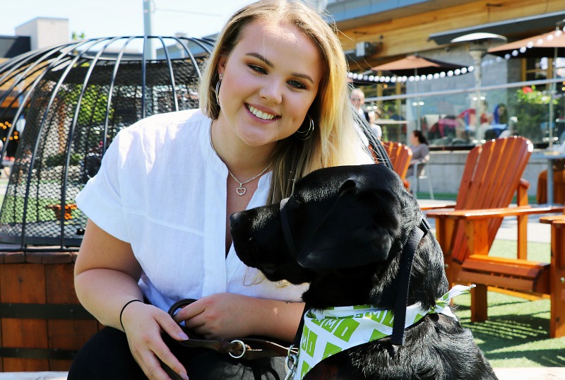 A woman and her guide dog smile into the camera.