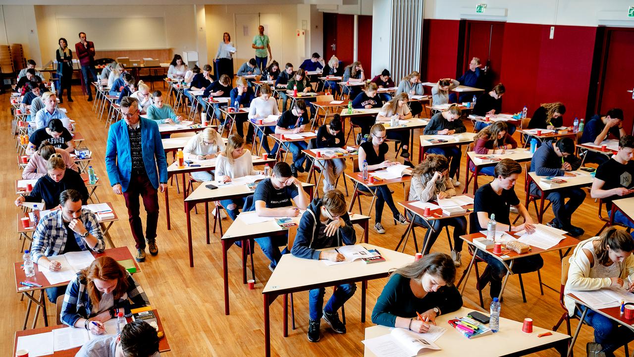 A large room full of rows of students doing exams. 