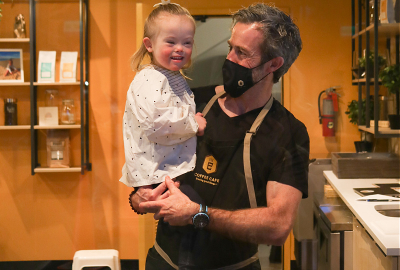 A man, wearing a surgical mask, holds a small girl in her arms.