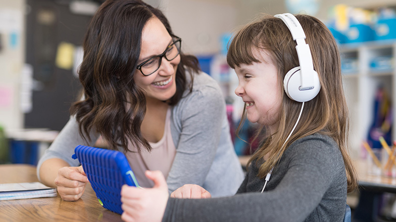 A little girl and a teacher playing on an ipad