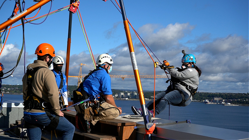 Jillian Gillis, tethered to a rope system, begins to climb down a building.