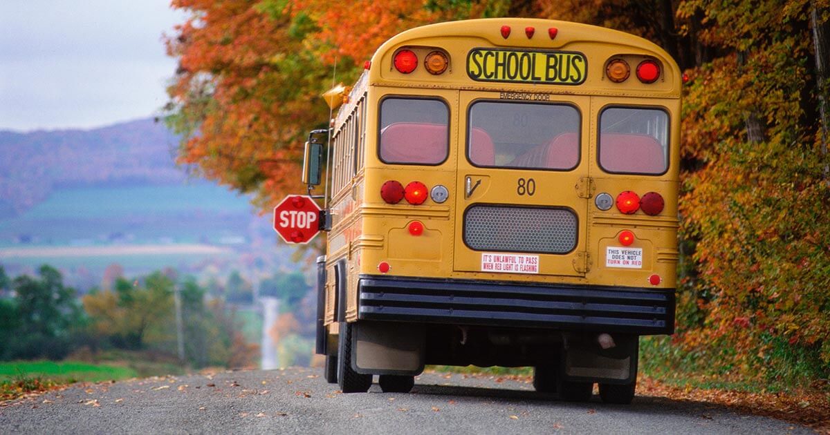 A school bus stops on a country road in autumn.