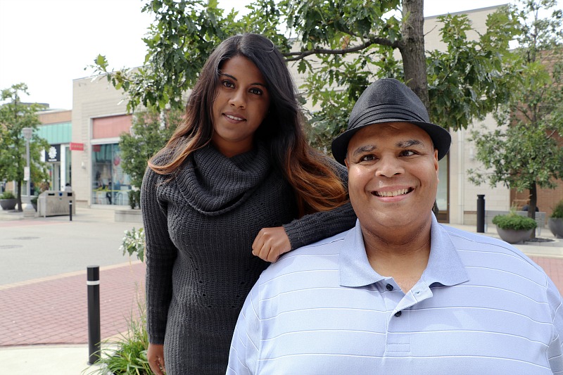 A man and a woman stand outside, smiling into the camera.